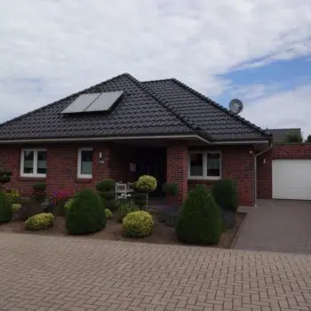 Foto eines roten Backstein-Bungalows mit dunklem Ziegeldach, Solarmodulen und gepflegtem Vorgarten.