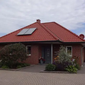 Ein Bungalow mit rotem Ziegeldach und Solarzellen, umgeben von einem gepflegten Garten mit Blumen