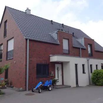 Ein modernes, zweistöckiges Backsteinhaus mit dunklem Dach und einem blauen Go-Kart davor.