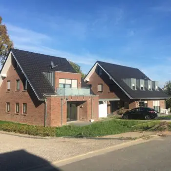 Ansicht von zwei modernen Doppelhaushälften mit dunklen Dächern und roten Backsteinfassaden unter blauem Himmel.