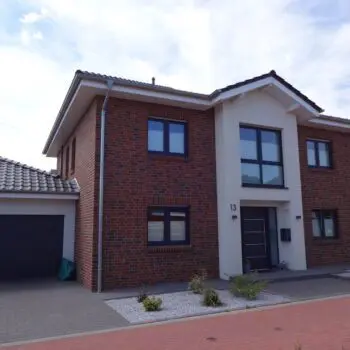 Ansicht eines modernen Einfamilienhauses (EFH) mit Garage, roter Backsteinfassade und dunklen Fensterrahmen unter blauem Himmel.