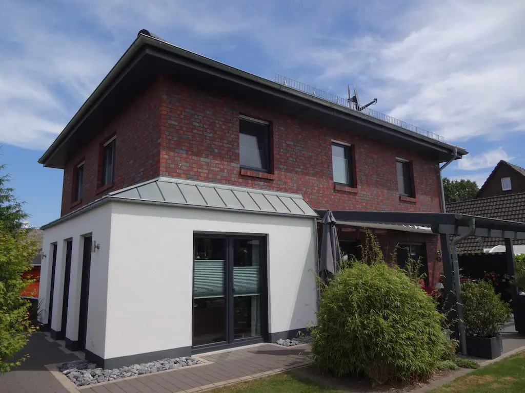 EFH-13: Ansicht eines zweistöckigen Einfamilienhauses mit roter Backsteinfassade und weißem Anbau unter blauem Himmel.