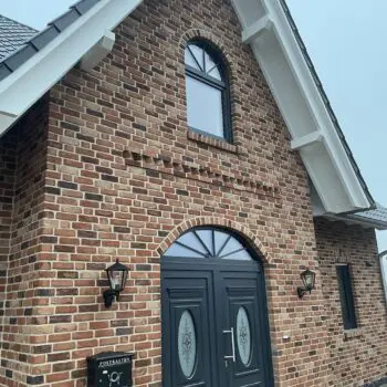 EFH: Fassade eines Hauses mit Backsteinen, Doppeltür, Fenster mit Bogen und Briefkasten.