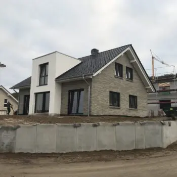 EFH-21: Ansicht eines modernen Einfamilienhauses mit Satteldach und weißem Anbau, Teil einer Neubausiedlung.