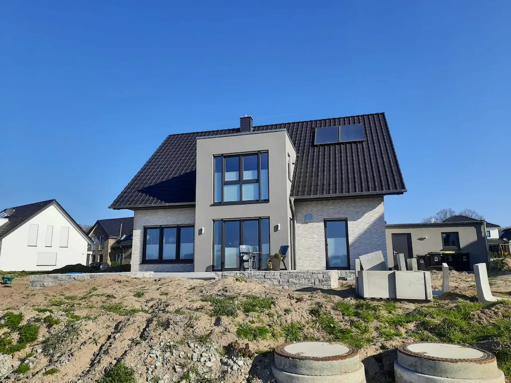 Modernes Einfamilienhaus (EFH-22) mit dunklem Ziegeldach und großen Fenstern unter blauem Himmel.
