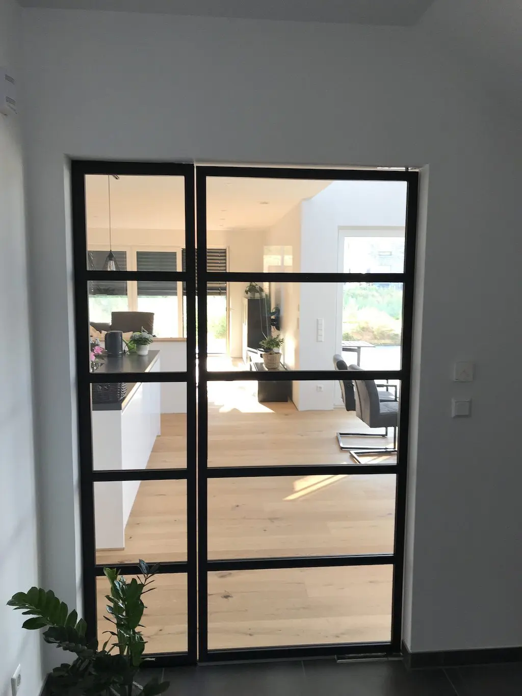 Moderne Innentür mit schwarzem Rahmen und Glas, Blick in Küche und Wohnbereich eines EFH