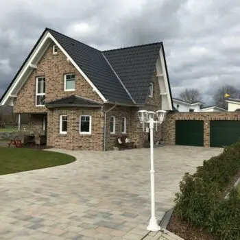 EFH-24: Ansicht eines Einfamilienhauses mit Garage, Backsteinfassade, dunklem Dach und gepflasterter Auffahrt.