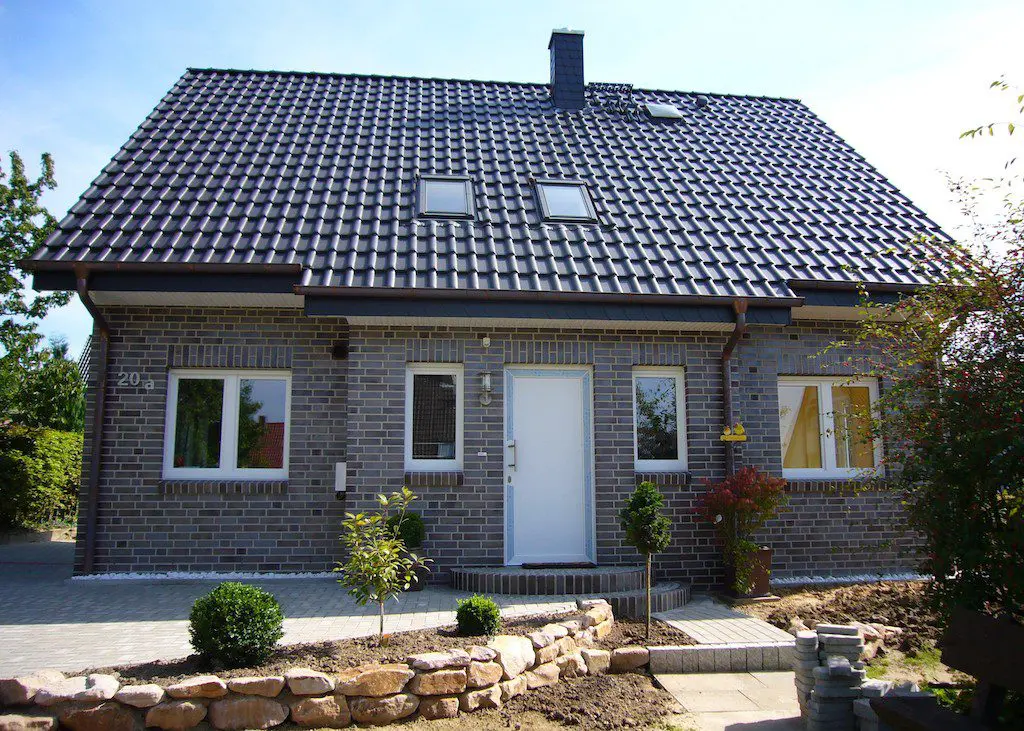EFH-26: Modernes Einfamilienhaus mit dunklem Ziegeldach und grauer Fassade, umgeben von einem gepflegten Garten.
