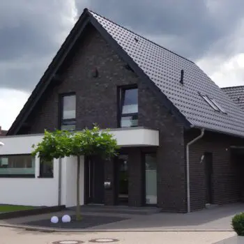 EFH-4: Modernes Einfamilienhaus mit dunkler Ziegelsteinfassade und Satteldach unter bewölktem Himmel.