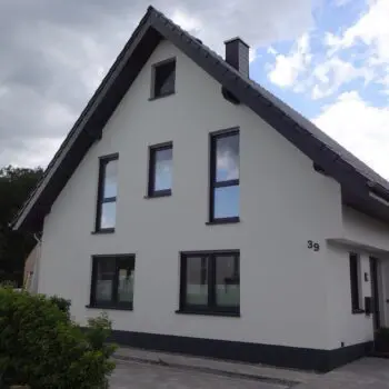 EFH-Hausansicht: Modernes Einfamilienhaus mit grauen Fensterrahmen und Giebeldach unter bewölktem Himmel.
