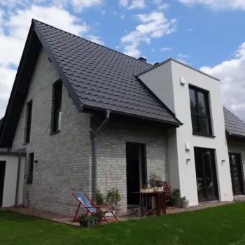 Ansicht eines modernen Einfamilienhauses (EFH) mit grauem Ziegeldach und Fassade aus weißem Stein auf einer Rasenfläche.