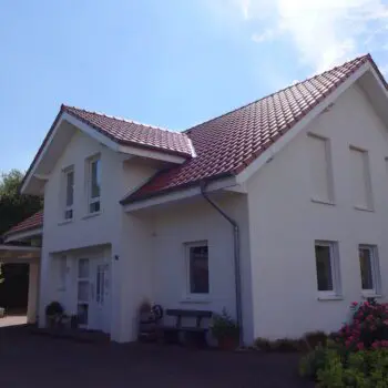 EFH-7: Ansicht eines weißen Einfamilienhauses mit rotem Ziegeldach und Garage an einem sonnigen Tag.
