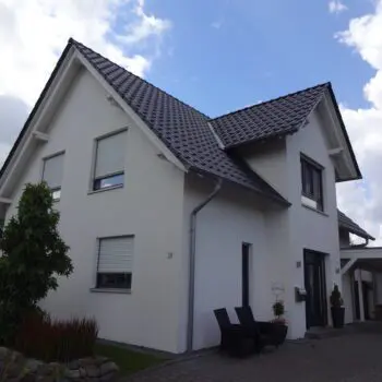 Ansicht eines modernen, zweistöckigen Einfamilienhauses mit dunklem Dach und weißen Fassade.