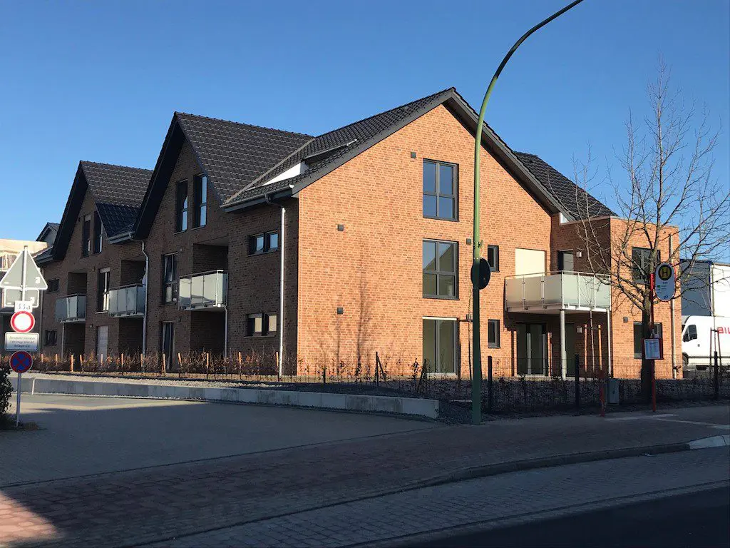 Foto von einem modernen Wohngebäude mit roten Ziegeln, dunklem Dach und Balkonen unter blauem Himmel.