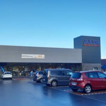 Außenansicht eines ALDI-Marktes mit Parkplatz und geparkten Autos vor dem Gebäude,Hinweisschild "Große Neueröffnung"