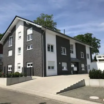 Ansicht eines modernen Mehrfamilienhauses (MFH) mit dunkler Backsteinfassade und weißen Elementen unter blauem Himmel.