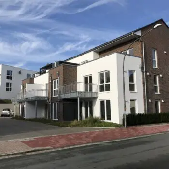 Mehrfamilienhaus mit modernen Balkonen und Parkplätzen vor blauem Himmel