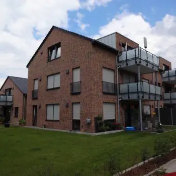 Mehrfamilienhaus: Rote Backsteinfassade mit Balkonen und Rollläden, umgeben von Rasenfläche.