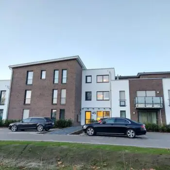 Modernes Mehrfamilienhaus (MFH) mit zwei geparkten Autos vor dem Gebäude.