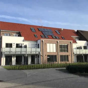 Ansicht eines Mehrfamilienhauses mit rotem Ziegeldach und Solarzellen auf dem Dach