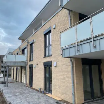Ansicht eines Mehrfamilienhauses mit gelben Ziegeln, Balkonen und grauer Pflasterung.