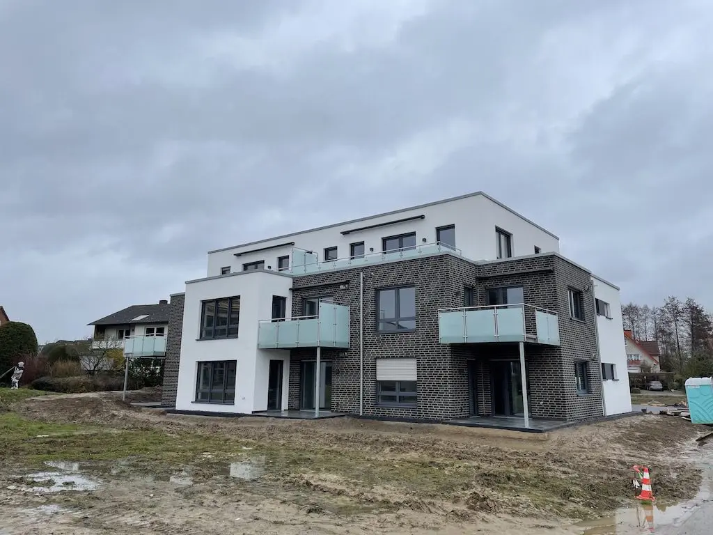 Modernes Mehrfamilienhaus (MFH-32) mit Balkonen und grauer Fassade unter bewölktem Himmel.