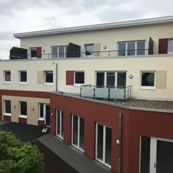 Ansicht eines mehrstöckigen Gebäudes, Fassade in Beige- und Rottönen, mit Balkonen und Fenstern.