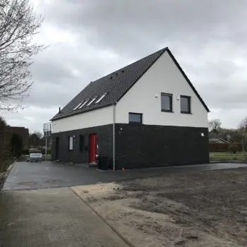 Ansicht eines modernen Einfamilienhauses mit dunklem Ziegelunterbau und weißer Fassade unter einem bewölkten Himmel.