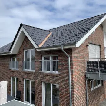 Ansicht eines modernen zweistöckigen Hauses mit Ziegelfassade, dunklem Dach und Balkonen.