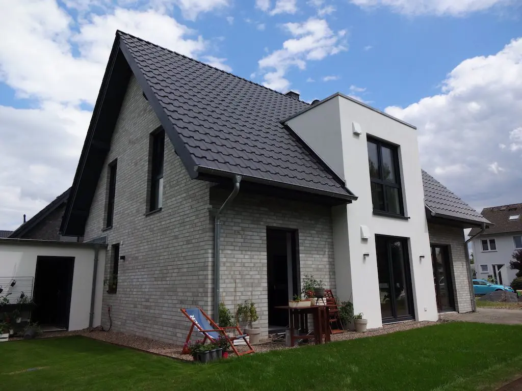 Ansicht des modernen EFH 'Lotte' mit heller Klinkerfassade und einem weißen Anbau unter blauem Himmel.