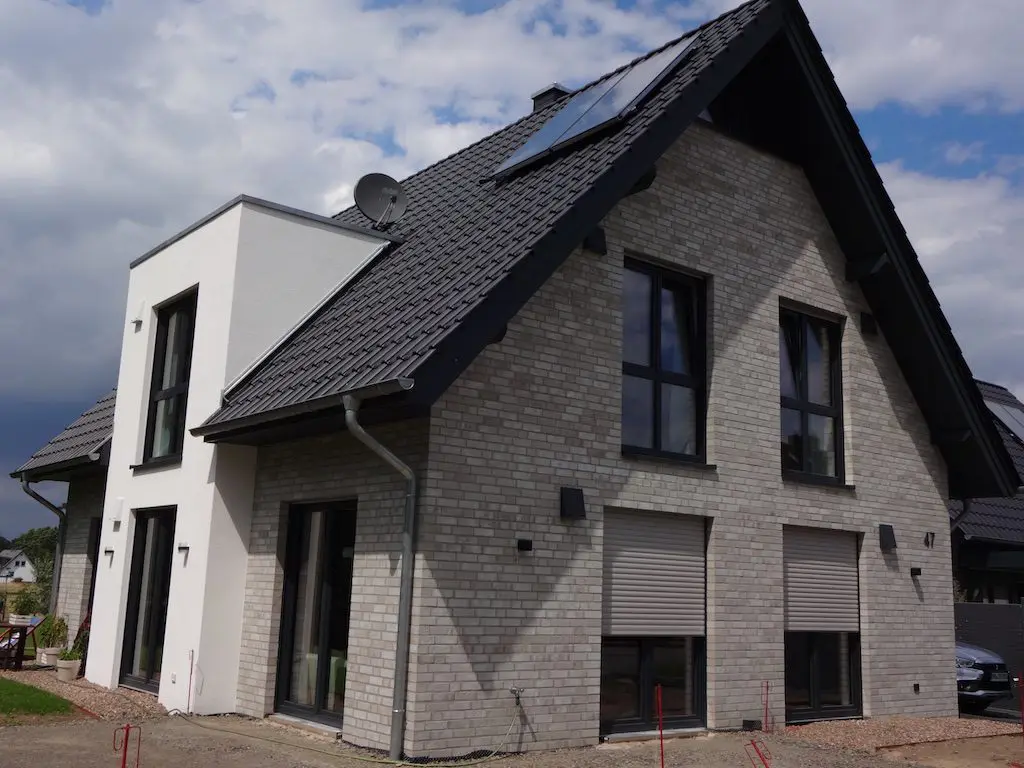 Dieses 'Lotte' Einfamilienhaus (EFH) präsentiert sich mit grauer Backsteinfassade, dunklen Fensterrahmen und Rollläden.
