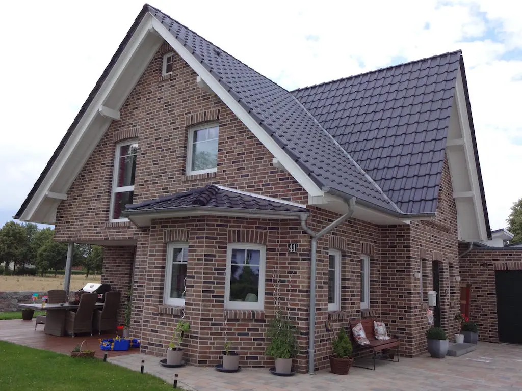 Außenansicht eines gepflegten Einfamilienhauses 'Lotte' mit dunklem Dach und einer Fassade aus braunem Backstein.