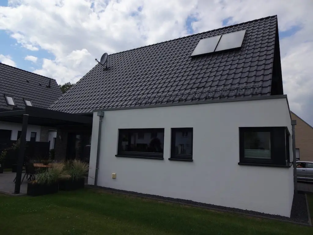 Detailaufnahme des 'Lotte' Einfamilienhauses: Weiße Fassade, dunkles Dach mit Solarpanelen und Fenster mit dunklen Rahmen.