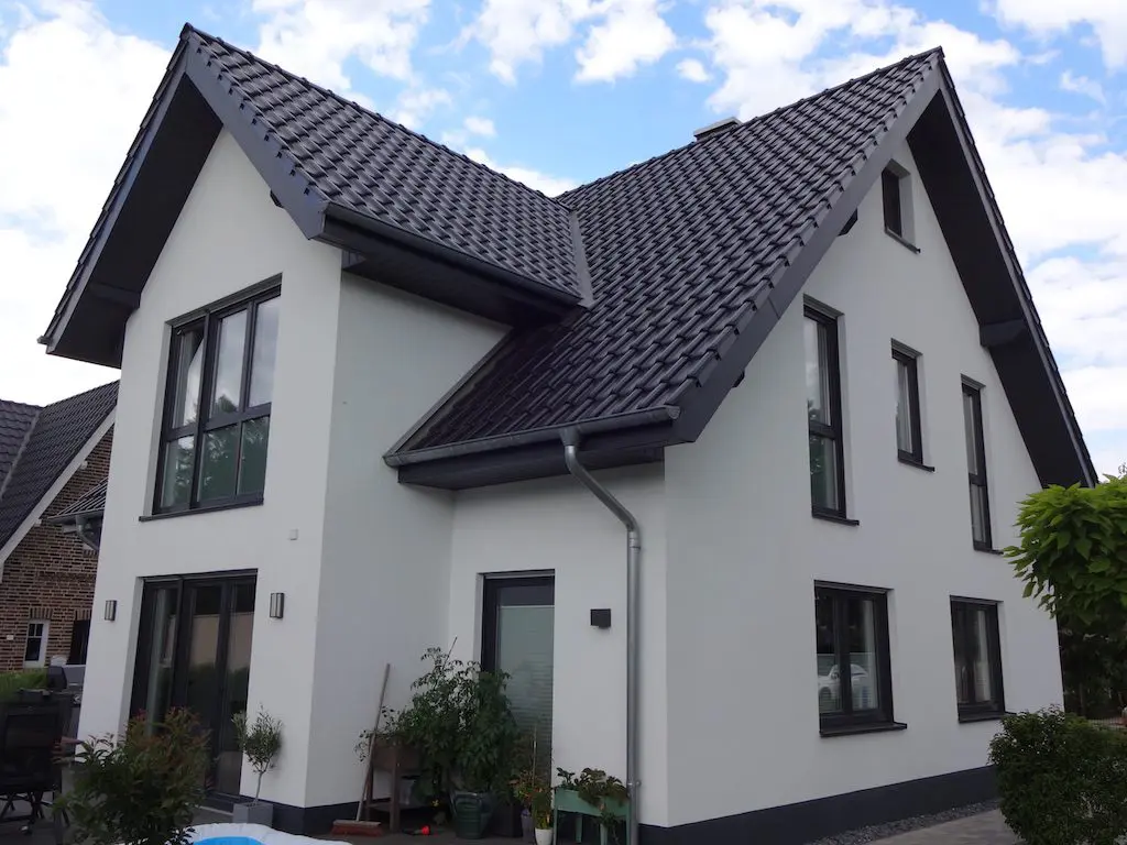 Ansicht eines modernen Einfamilienhauses (EFH) mit dunklem Ziegeldach und weißen Fassadenputz.