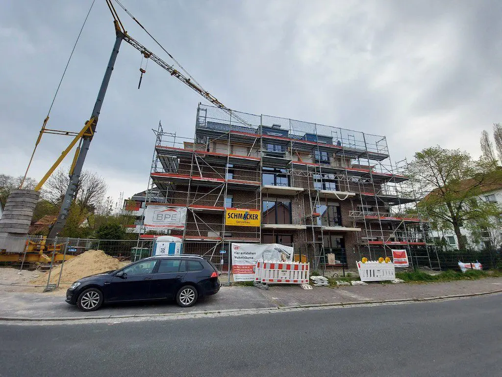 Neubau mit Gerüst und Kran im Bauprozess, Baustelle mit Stapel von Beton-Gewichten und einem Auto davor.