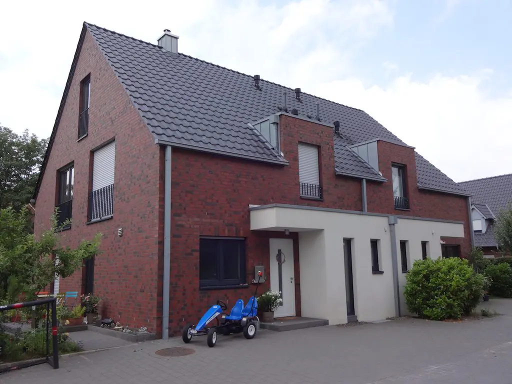 Frontansicht eines Reihenhauses (Wasserweg 106-112) mit roter Backsteinfassade, weißem Anbau und blauem Gokart davor.