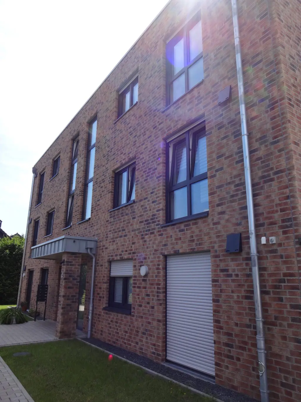 Fassade eines Mehrfamilienhauses, gebaut aus roten Ziegelsteinen, mit Rolltor und modernen, dunklen Fensterrahmen.