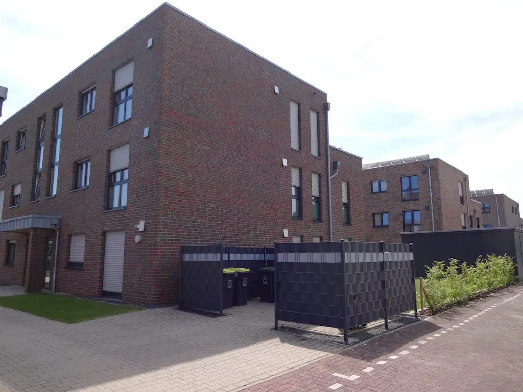Mehrfamilienhäuser mit roten Ziegelsteinen, Mülltonnenbox und gepflastertem Gehweg im Außenbereich.