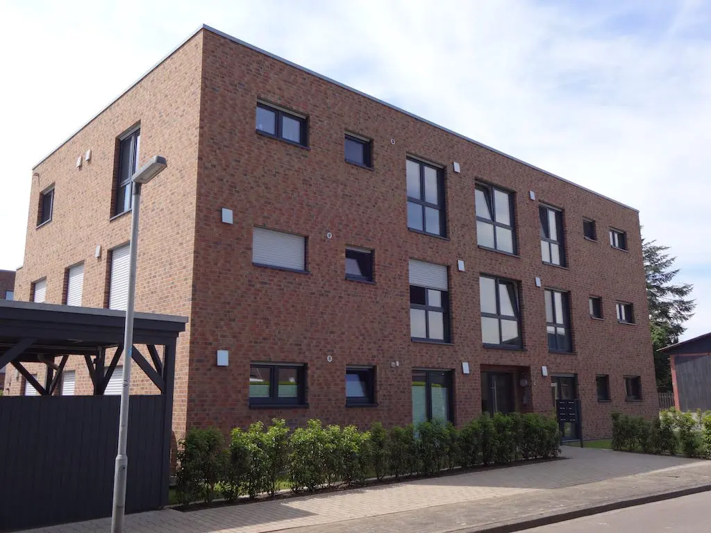 Außenansicht eines modernen Mehrfamilienhauses mit Fassade aus roten Ziegelsteinen und dunklen Fensterrahmen.