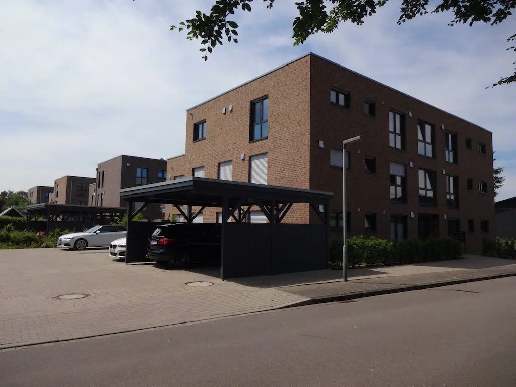 Mehrfamilienhäuser mit Carports und gepflasterten Stellplätzen. Zu sehen sind Ziegelbauten mit dunklen Fensterrahmen.