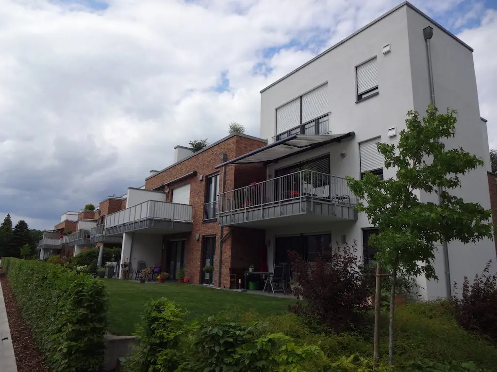 Reihe von modernen Wohnhäusern mit Balkonen und gepflegten Gärten unter bewölktem Himmel.