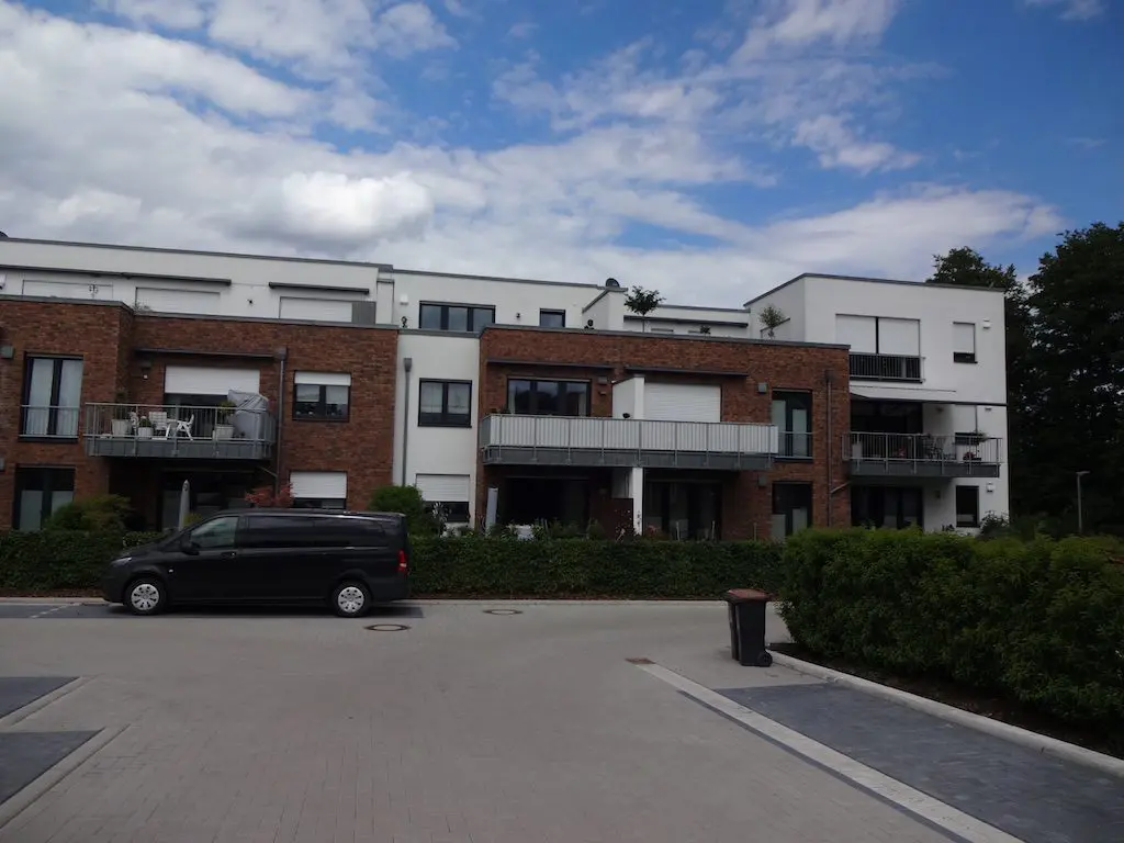 Mehrfamilienhaus mit Backsteinfassade, Balkonen und einem geparkten schwarzen Lieferwagen vor dem Gebäude.