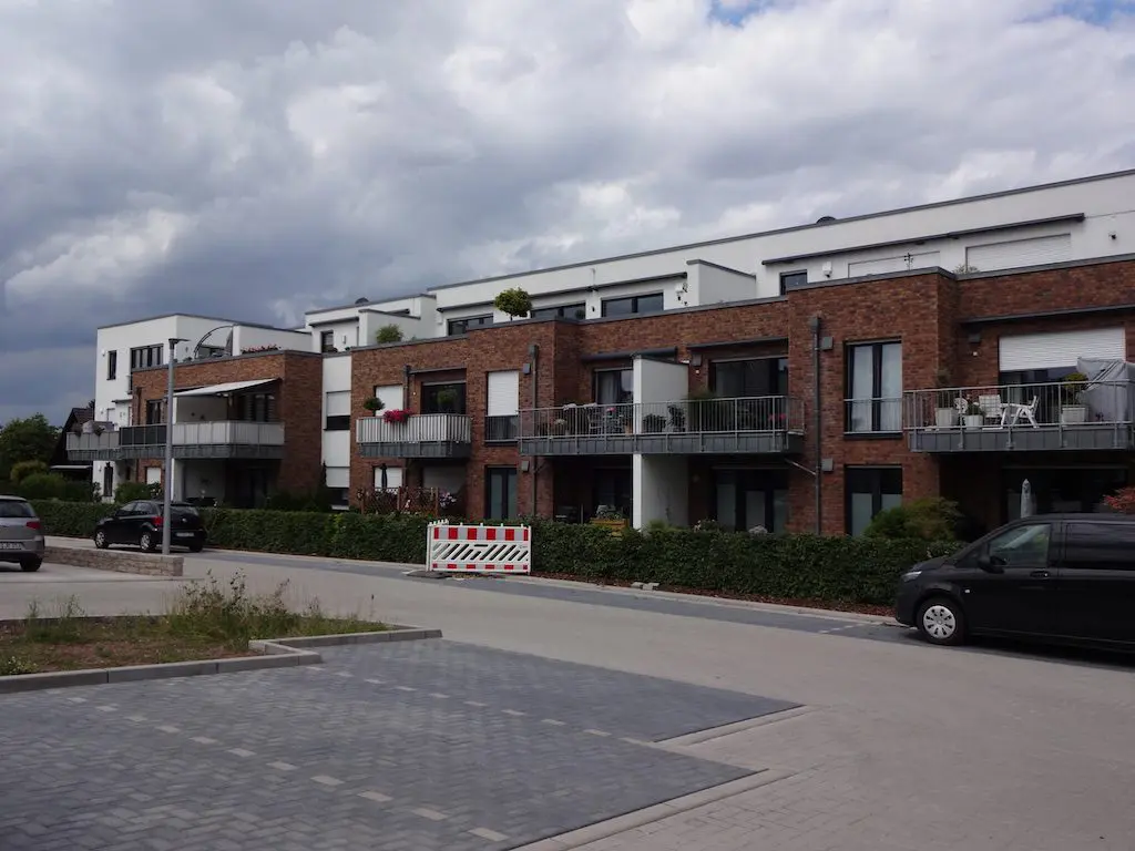 Moderne Wohngebäude mit Balkonen und gepflegter Außenanlage unter bewölktem Himmel.