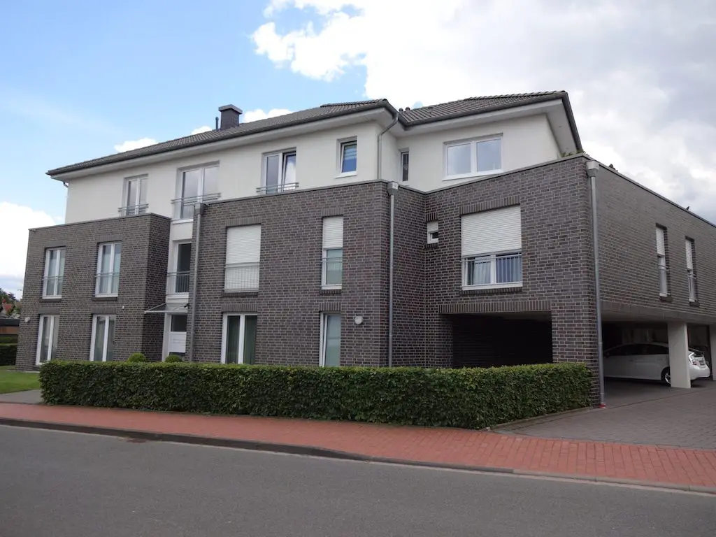 Ansicht eines modernen Mehrfamilienhauses mit Garage, gebaut aus Backstein und Putz unter blauem Himmel.