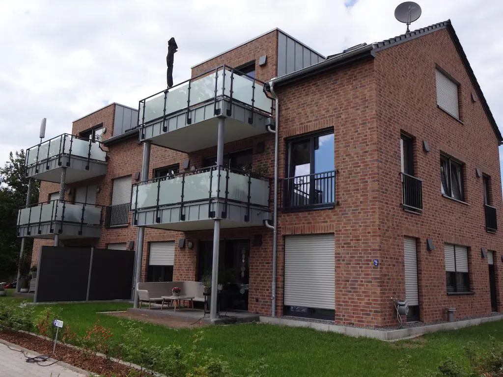 Mehrfamilienhaus aus Backstein mit Balkonen und Rollläden. Satellitenschüssel auf dem Dach.