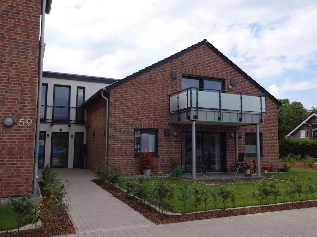 Ansicht eines modernen Backsteinhauses mit Balkon und gepflegtem Garten, aufgenommen bei Tageslicht.