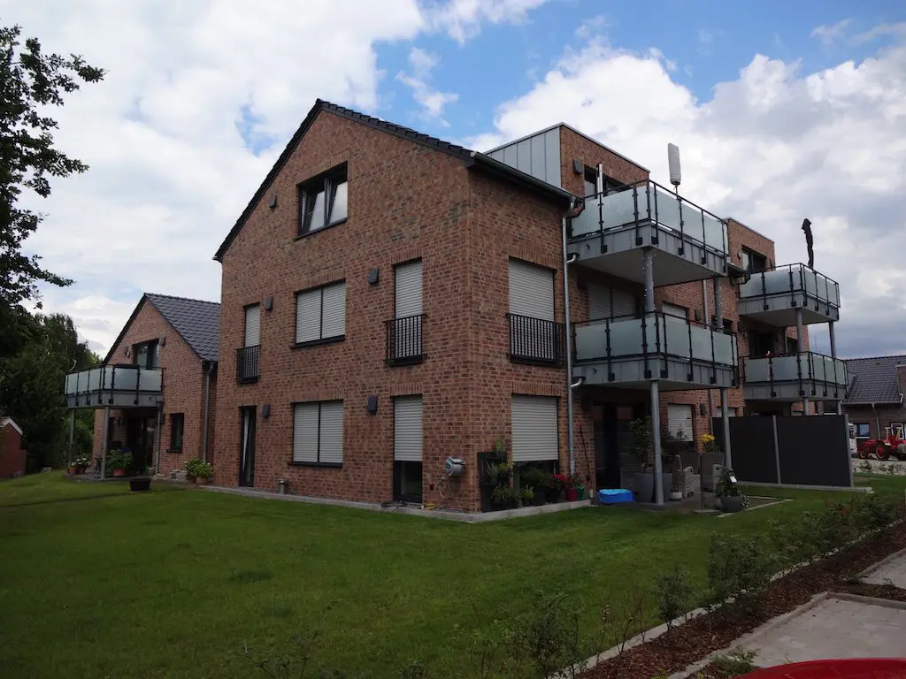 Ansicht eines modernen Mehrfamilienhauses mit Backsteinfassade und Glasbalkonen, umgeben von Rasenflächen.
