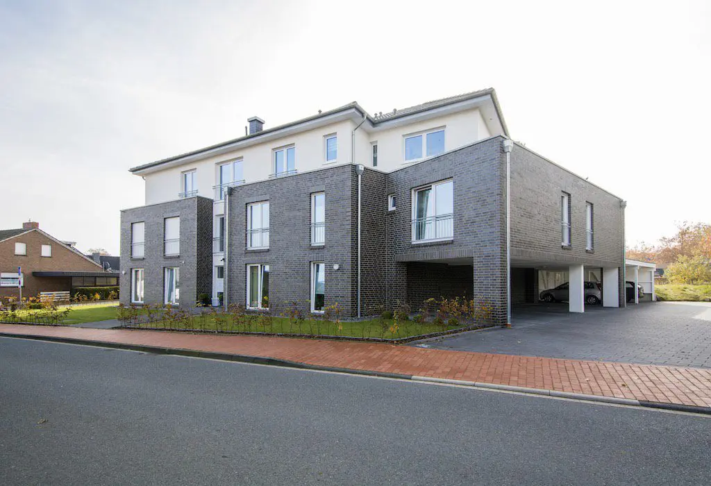 DSC7159: Modernes Mehrfamilienhaus mit grauer Backsteinfassade und Stellplätzen im Erdgeschoss.