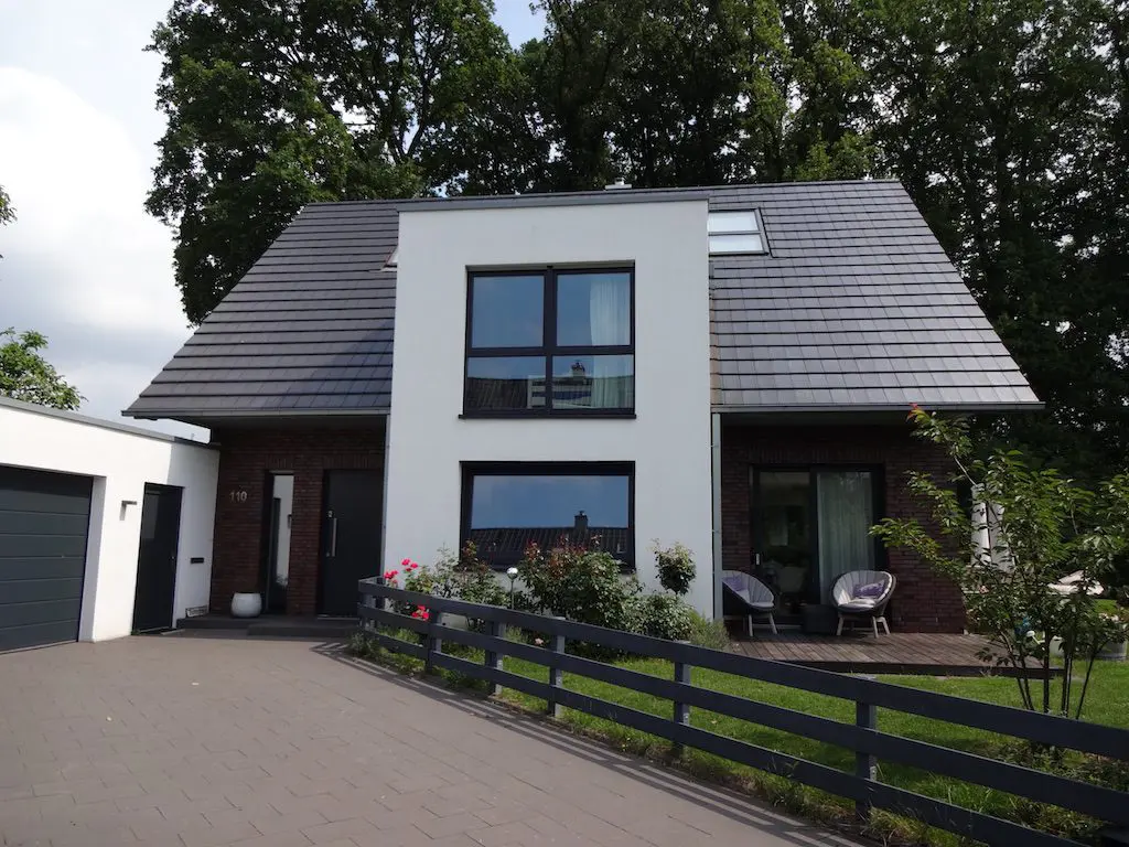 Darstellung eines modernen EFH mit weißer Fassade, dunklem Ziegeldach und gepflasterter Einfahrt, Wasserweg-Reihenhaus.