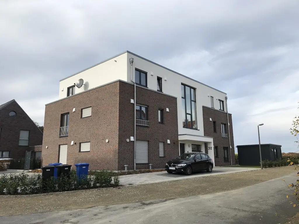 IMG_3013.jpg: Ansicht eines modernen Mehrfamilienhauses mit dunklem Auto vor dem Gebäude.